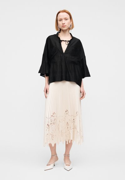 Μαύρο, φαρδύ μπλούζα με V-λαιμόκοψη και φαρδιά μανίκια. Συνδυασμένη με πλισέ κρεμ φούστα με ανθοκομμένες λεπτομέρειες.