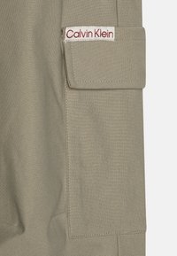 Calvin Klein cargo byxor i ljusbeige tyg, med en ficka med lock, broderad logotyp och vertikal ribbad textur.