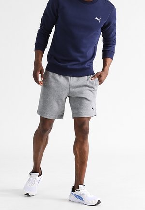 Sudadera marina con puños y dobladillo acanalados, combinada con pantalones cortos grises. Logo de Puma en blanco en ambas prendas. Zapatillas blancas con acentos azules.