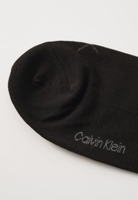 Fekete pamut zokni bordázott kialakítással, kerek orral és egy kis szürke "Calvin Klein" logóval az oldalán.