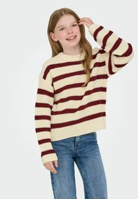 Cream and burgundy striped knit sweater with a round neckline, ribbed sleeves, and a loose fit, paired with blue denim jeans.