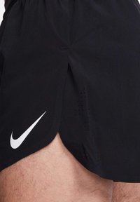 Shorts de sport noirs avec fente sur le côté, arborant un logo Nike blanc. Fabriqués en tissu léger avec des détails perforés pour une meilleure respirabilité.