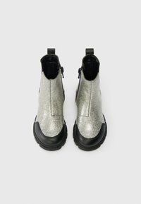 Strieborné trblietavé členkové čižmy s čiernou gumovou podrážkou a špičkou, vybavené predným zipsom a elastickými bočnými panelmi pre jednoduché obúvanie.