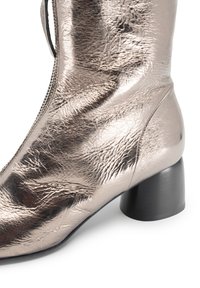 Stivale alla caviglia in argento metallico con superficie testurizzata, chiusura con cerniera e tacco massiccio nero. Il design presenta una silhouette liscia.