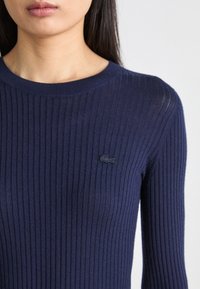 Maglione a coste blu navy con scollatura rotonda, caratterizzato da un piccolo logo scuro sul petto e maniche lunghe e aderenti.
