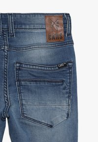 Džínové kalhoty s bledě modrým praním, kožený logo štítek s nápisem "CARS" a zadní kapsa s vyšitými detaily a malou cedulkou.