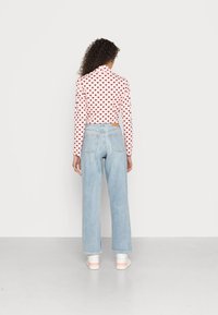 Blusa de manga comprida rosa claro com padrão de pequenos corações vermelhos, combinada com calças de ganga largas azul claro. Detalhe notável: etiqueta de ganga na parte de trás.