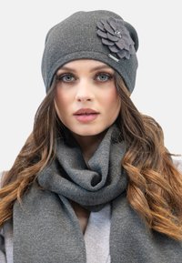 Cappello di lana grigio con un accento di fiore in tessuto e una sciarpa spessa grigia. Le trame sono morbide e si adattano bene. I colori sono tenui e si completano a vicenda.