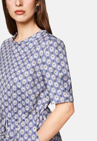 Blau gemustertes Kleid mit kurzen Ärmeln, elastischem Bund und komplizierten floralem Design mit kontrastierenden schwarzen Akzenten.