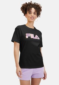 Camiseta de algodón negra con un llamativo logo "FILA" en rosa y morado. Manga corta, cuello redondo y un corte relajado. Diseño simple y textura suave.