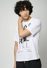 T-shirt en coton blanc avec un texte graphique et des chiffres noirs. Manches courtes, coupe décontractée, avec des coutures visibles et un col arrondi.