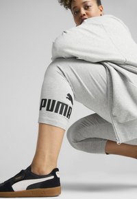 Szürke cipzáras kapucnis pulóver, széles ujjakkal, szürke sportnadrággal párosítva, melyen fekete "PUMA" felirat található a bokánál, fekete sportcipőkkel, fehér kiegészítőkkel.}}