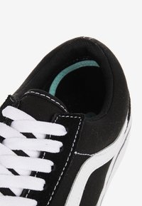 Baskets en toile noires avec lacets blancs, rayure blanche contrastante, col rembourré et semelle extérieure texturée noire. L'intérieur présente des accents bleu clair.