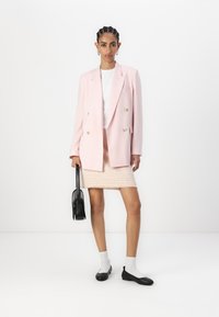 Svetle růžový dvouřadý blazer přes bílou košili, doplněný pastelově růžovou tweedovou sukní. Černá kabelka, bílé ponožky a černé boty.