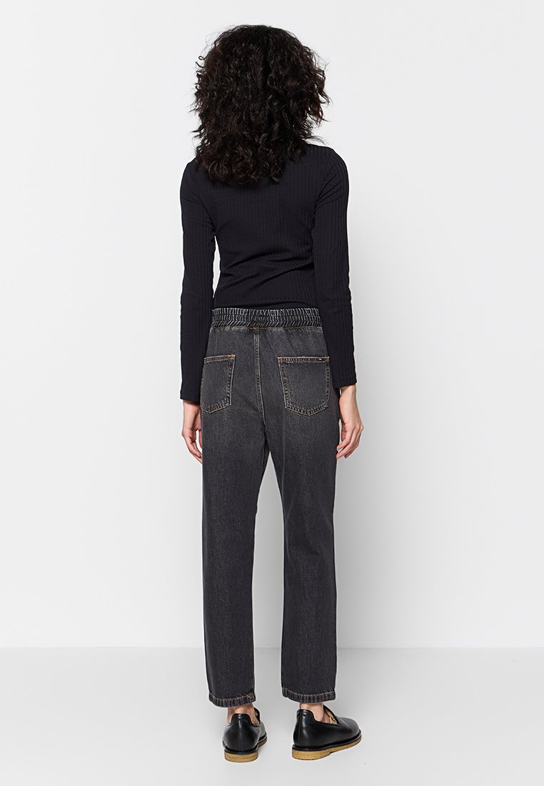 Top lungo a maniche lunghe nero a costine abbinato a jeans grigi scuri a gamba dritta a vita alta, con cintura elastica e tasche posteriori.