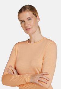 Ljus orange långärmad topp med rund halsringning, tillverkad av ett slätt tyg, med långa ärmar och en figurnära design.