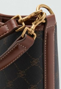 Sac noir à motifs avec des accents en cuir marron. Dispose de quincaillerie et de coutures dorées. Sa forme est carrée avec un design structuré.