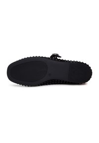 Semelle plate noire avec une surface antidérapante texturée et de petites pastilles rondes le long du bord, dotée d'une bride à boucle sur le dessus.