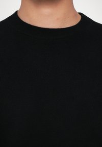 Sort crewneck jumper i blødt strikket stof med ribbet krave og glat tekstur uden synlige mønstre eller detaljer.