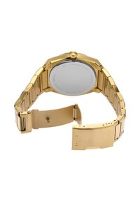Reloj de pulsera de metal con tono dorado con cierre abierto, caja trasera visible grabada con detalles de la marca y el material.