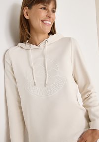 Beżowa bluza z kapturem z teksturowanym logo przedstawiającym góry oraz frazę "NOWA DROGA". Sznurki z metalowymi końcówkami, miękka tkanina.