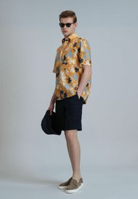 Korte mouwen graphic shirt in oranje met een blauw en zwart bloemenpatroon, gecombineerd met donkere shorts en beige instappers.