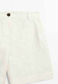 Close-up of cream-colored shorts with a button closure, belt loop, and side pocket visible on a plain background.