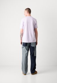 Lilac short-sleeve t-shirt paired with two-tone baggy denim pants, featuring different shades and patch pockets. Brown footwear visible.