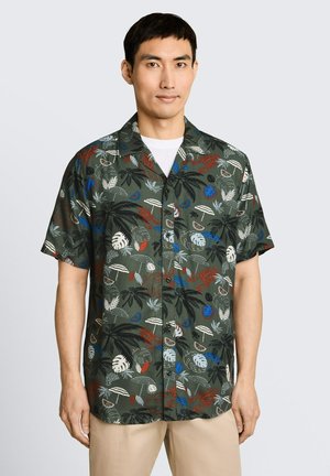Man wearing short-sleeve button-up shirt with tropical print of palm leaves, umbrella motifs, and seafood in green, blue, white, and red tones.