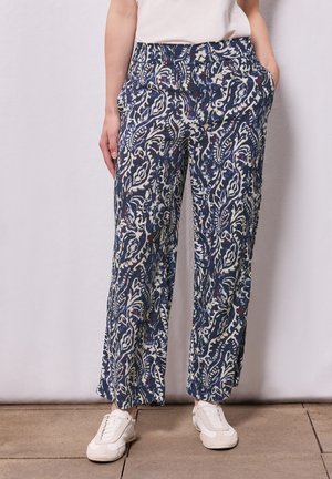 Marineblaue gemusterte Hosen mit floralem Design, im entspannten Schnitt, mit Taschen und aus leichtem Stoff, kombiniert mit weißen Sneakern.