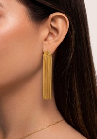 Gouden franjen oorbellen met een gebogen bovenkant en lange, gelaagde strengen die naar beneden vallen. Gladde textuur, lichtgewicht ontwerp en elegante afwerking.