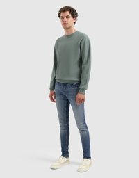 Getextureerde lichtgroene trui met een ronde hals, gecombineerd met slim-fit blauwe jeans en beige sneakers; eenvoudig ontwerp met ribbelmanchetten.
