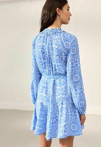 Abito blu con motivo floreale, maniche lunghe, colletto arricciato e gonna svasata. Realizzato in tessuto leggero. Caratterizzato da un design intricato.