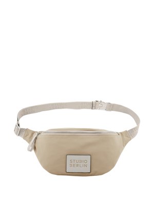 Beige Bauchtasche mit Reißverschluss und verstellbarem Riemen, mit dem Text "STUDIO BERLIN" auf dem vorderen Aufnäher und dem Riemen.
