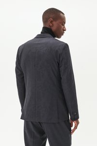 Chaqueta de traje de patrón oscuro con un corte entallado, que presenta un cuello de muesca y puños abotonados. Textura de tela suave, diseño elegante.