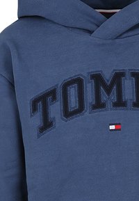 Felpa blu realizzata in un tessuto misto cotone, con una grande scritta nera "TOMMY" e un piccolo logo rosso, bianco e blu in basso.
