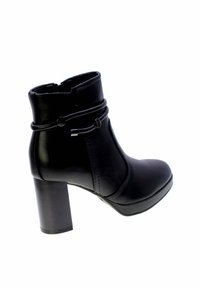 Stivale alla caviglia in pelle nera con tacco alto chunky, cinturino decorativo avvolgente con dettagli in metallo e chiusura con cerniera laterale.