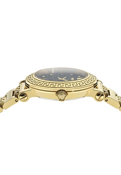 Zlato obarvan ročni računalnik s črnim vzorčastim številčnikom, geometrijskim oblikovanjem okvirja ter glavo Meduze na kroni in povezavah naramnice.