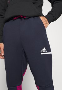 Marina atletiska byxor med en strukturerad yta, med rosa detaljer och en vit Adidas-logotyp på vänster lår. Inkluderar framfickor och dragsko i midjan.