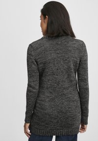 Pull en tricot gris avec de longues manches, un col rond et un ourlet côtelé. La texture semble douce avec un motif chiné subtil.