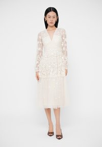 Rochie midi albă cu mâneci lungi transparente, broderie florală, decolteu în V și fustă stratificată din tul. Material neted cu textură delicată.