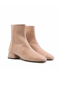 Botas de cuero nude hasta el tobillo con punta afilada y tacón bajo. Textura suave con costuras mínimas y una silueta elegante.