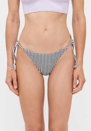 Bikini onderkant in zwart-wit ruitpatroon met verstelbare strikjes aan de zijkanten. Gemaakt van gladde stof, biedt minimale bedekking.