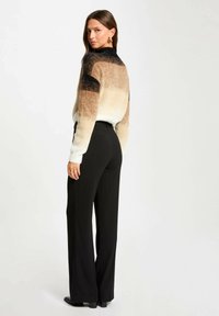 Suéter de punto con tonos degradados de marrón y crema, con un escote alto. Combinado con pantalones de pierna ancha negros y botas hasta el tobillo.