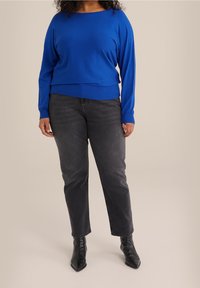 Blue knit sweater with a wide neckline, long sleeves, and a fitted hem, paired with black jeans and pointed black ankle boots.