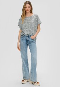 Kurzarmtop mit Floral-Muster in Hellblau, kombiniert mit hellen, weit geschnittenen Jeans und cremefarbenen Plattformsandalen.