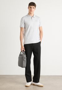 Polo cinza claro, calças pretas e ténis brancos. Saco de mão cinza, textura suave, logotipo discreto na camisa. Fundo neutro.