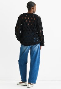 Black knitted sweater with large open weave pattern, paired with loose blue denim jeans and silver flat shoes. Back view of the outfit.