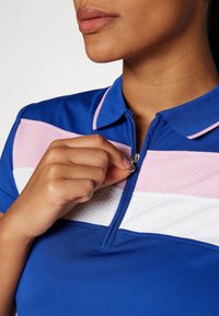 Polo shirt blu con colletto zip, con strisce testurizzate rosa e bianche. Tessuto liscio con un design aderente, che mette in risalto il décolleté.