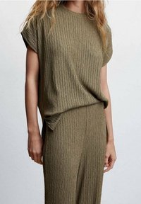 Haut en vert olive texturé avec des manches courtes et une coupe décontractée, présentant de légères rayures verticales. Assorti avec un bas texturé assorti.